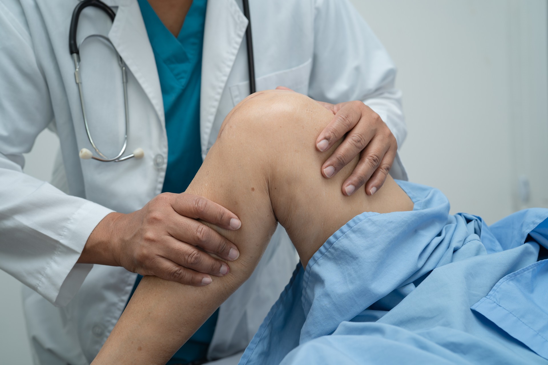 Asian doctor physiotherapist examining, massaging and treatment knee and leg of senior patient in orthopedist medical clinic nurse hospital.